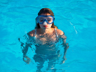 Naklejka premium Cute happy young girl in goggles swimming and snorking in the swimming pool