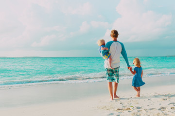 father and two little daughter walk on beach