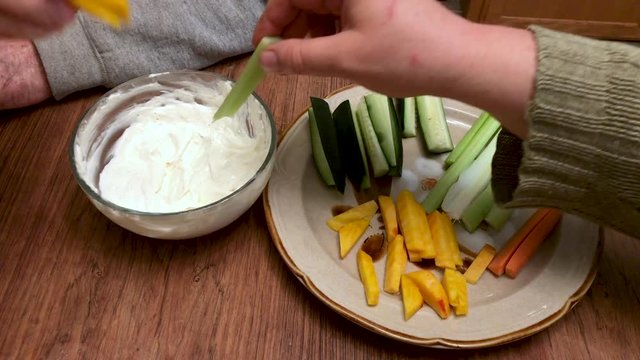 Organic vegetables and ranch dip on a home table. Male and female hands dipping veggies in sour cream