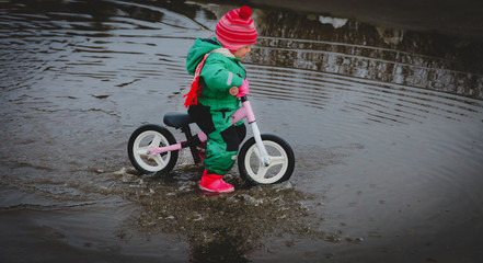 little girl riding bike in spring water puddle