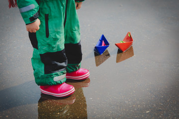 little girl playing with paper boats in water puddle