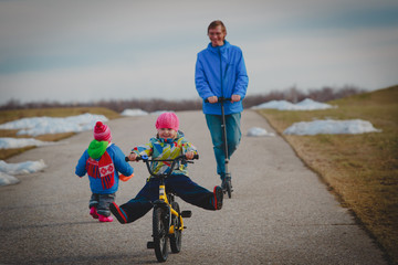 active spor family- father on schooter with kids outside, little girl on bike