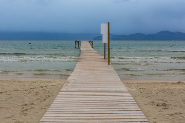 Heller Holzsteg führt über den Sandstrand ins wellige Meer hinaus, copy space