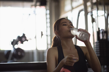 Fototapeta na wymiar Young athletic fitness woman drinking water from bottle in gym.