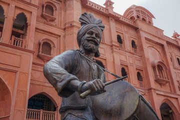 Statue of the drummer on the background of the red building. Amritsar, India