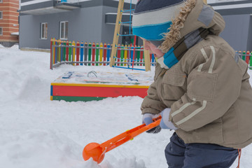Child makes snowballs orange snowglade in outdoor playground