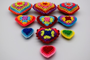Knitted hearts from a multi-colored yarn on a white background. Valentine's Day, love, handmade, amigurumi, hobby, decoration, postcard, creative.