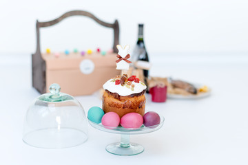 Easter cake, colored eggs and bottle of red wine. Easter composition with orthodox sweet bread, kulich and bottle of wine on light background. Gifts for holiday in wooden basket. Copyspace for text