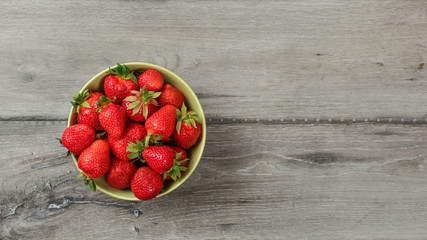 Top down view, small bowl with strawberries on gray wood desk. Space for text on right.