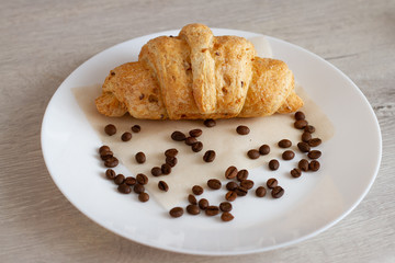 croissant and grains of coffee on a white plate