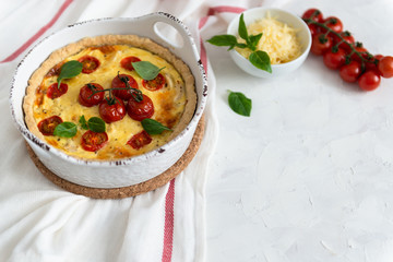Homemade tomato pie with basil leaves ans cheese on white tablecloth. Copy space