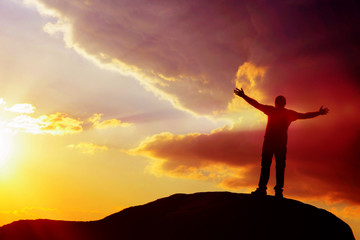 silhouette of a man on top of a mountain with his hands up at sunset. achieving goal.