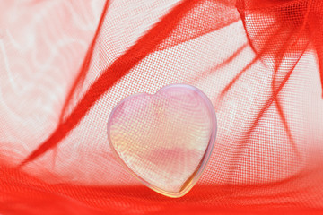 .Valentine's day. A small transparent plastic heart lies in a red transparent fabric.