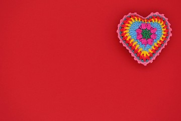 Knitted heart of colored yarn on a red background. Valentine's Day, love, handmade, amigurumi, hobby, decoration, postcard, creative.