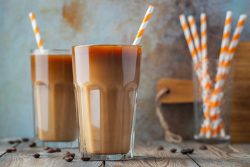 Ice coffee in a tall glass with cream poured over, coffee ice cubes and beans on a old rustic...
