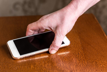 Hand picking up mobile phone from table. 