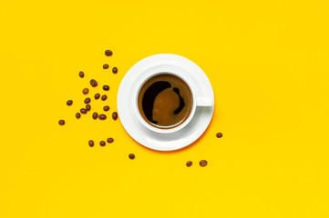 Flat lay cup of black coffee and coffee beans on yellow background top view copy space. Minimalistic food concept, morning breakfast, time to work, hot drink, coffee background