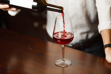 Male sommelier pouring red wine into long-stemmed wineglasses.