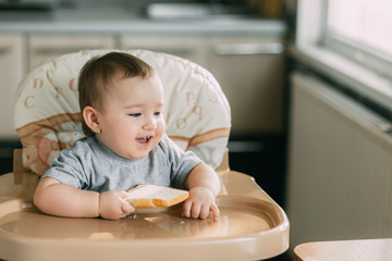 baby in the kitchen in the high chair there is a piece of bread