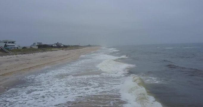 AERIAL: pushing perpendicularly to the direction of the crashing waves on the shoreline of East Quogue, New York on a foggy day.