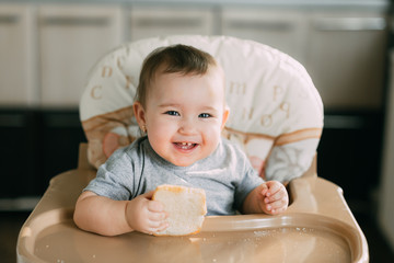 baby in the kitchen in the high chair there is a piece of bread