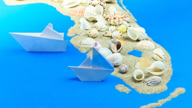 A paper boat sails off the coast of Florida. The contours of Florida lined with sand, on top - shells.