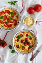 Tomato pies with basil leaves, chicken ans cheese on white tablecloth. Homemade french quiche. Top view