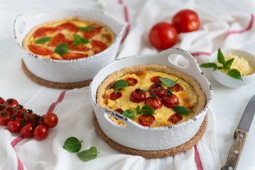 Tomato pies with basil leaves, chicken ans cheese on white tablecloth. Homemade french quiche. Top view