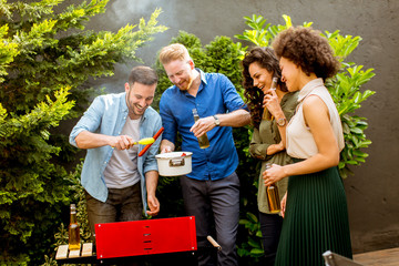 Happy friends grilling food and enjoying barbecue party outdoors