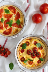 Tomato pies with basil leaves, chicken ans cheese on white tablecloth. Homemade french quiche. Top view