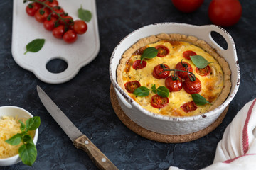 Homemade quiche with tomatoes, chicken, basil leaves and cheese on dark background. Close up