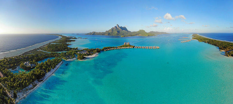 Aerial panoramic landscape view of the island of Bora Bora in French Polynesia with the Mont Otemanu mountain surrounded by a turquoise lagoon, motu atolls, re