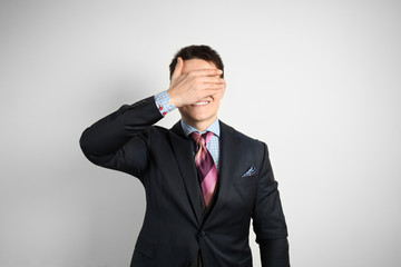 Young businessman in suit on gray background face palm and smiling.