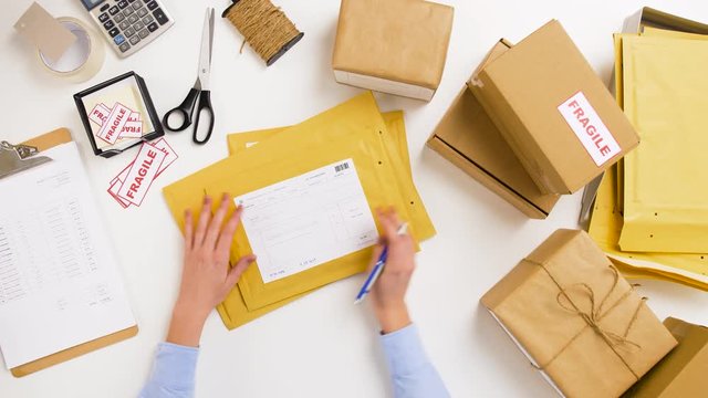 delivery, mail service, people and shipment concept - woman signing parcel envelopes at post office