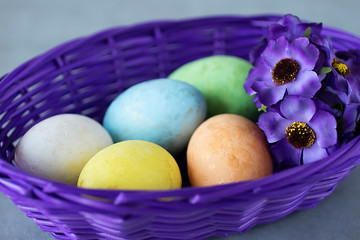 Five multicolored decorative eggs in a purple basket on a gray background. Easter concept.