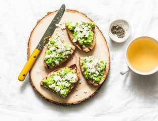 Avocado, goat cheese, grilled ciabatta sandwiches and green tea on light background, top view. Healthy breakfast or snack