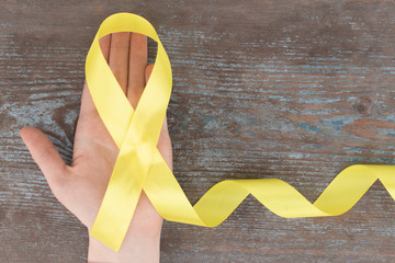 yellow ribbon-childhood cancer awareness symbol on the wooden background with copy space