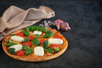 Italian pizza with Mozzarella cheese, tomatoes, broccoli, Spices and fresh basil. Pizza and kitchen napkin near, on black stone background