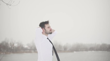 Businessman Looks Afar At Lake In Winter Sunrise. Man Looks Afar In Winter At Beach.Man Stands On Shore And Looks Into Distance.Mysterious Man Sitting On The Beach And Looks At River in Winter.  - Powered by Adobe