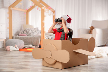 Cute little boy playing with binoculars and cardboard airplane in bedroom