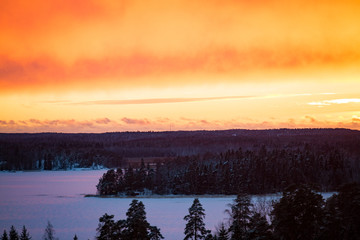 Dramatic sky above Baltic Sea. Orange, pink and purple colours of sunset. Aerial view on frozen gulf, lakes, forest and islands covered with snow. Finland in winter. 