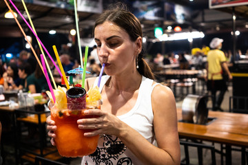 The girl drinks a big cocktail from a straw in a nightclub, a night cafe