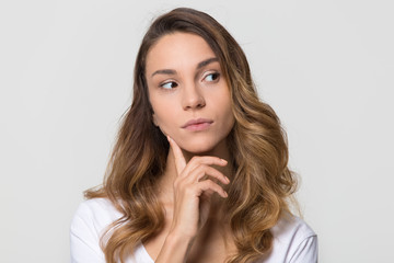 Thoughtful young woman looking away feeling doubt isolated on white studio wall, millennial girl...