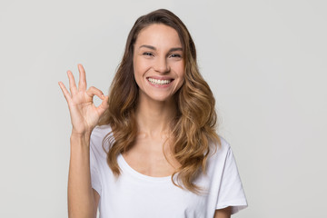 Happy woman gesturing ok smiling with white teeth looking at camera isolated on studio blank...