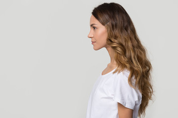 Young female millennial woman standing in profile on white grey background with copy free space for text, confident serious girl lady model isolated on blank studio wall, side view portrait