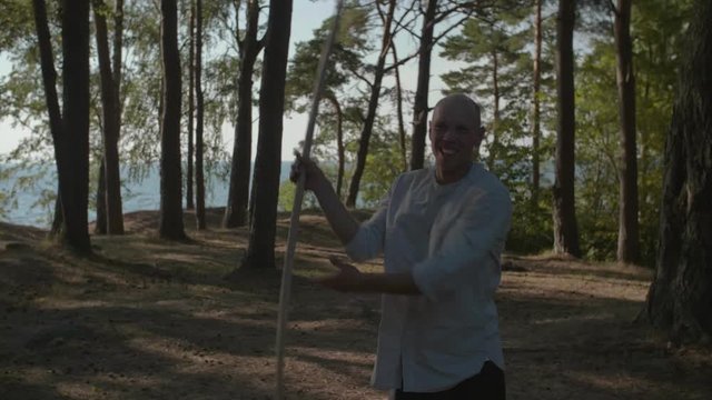 Martial artist practicing wushu staff routine in the forest in slow motion, 50 fps.