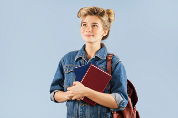 Obraz premium beautiful student girl in a denim jacket with a backpack on her shoulders in the studio on a blue background. The concept of education and learning.