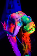 Female dancer in bright neon colours under ultraviolet light on background.