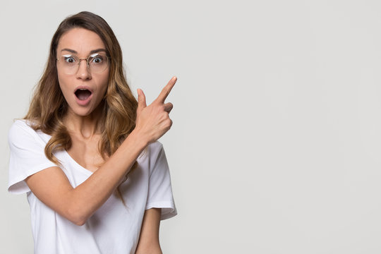 Amazed girl student wear optic glasses pointing finger at copy space looking at camera isolated on white studio blank background, surprised woman customer show aside advertise product service sale