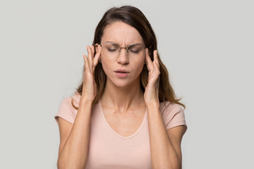Tired stressed young woman feeling strong headache massaging temples isolated on grey white blank...